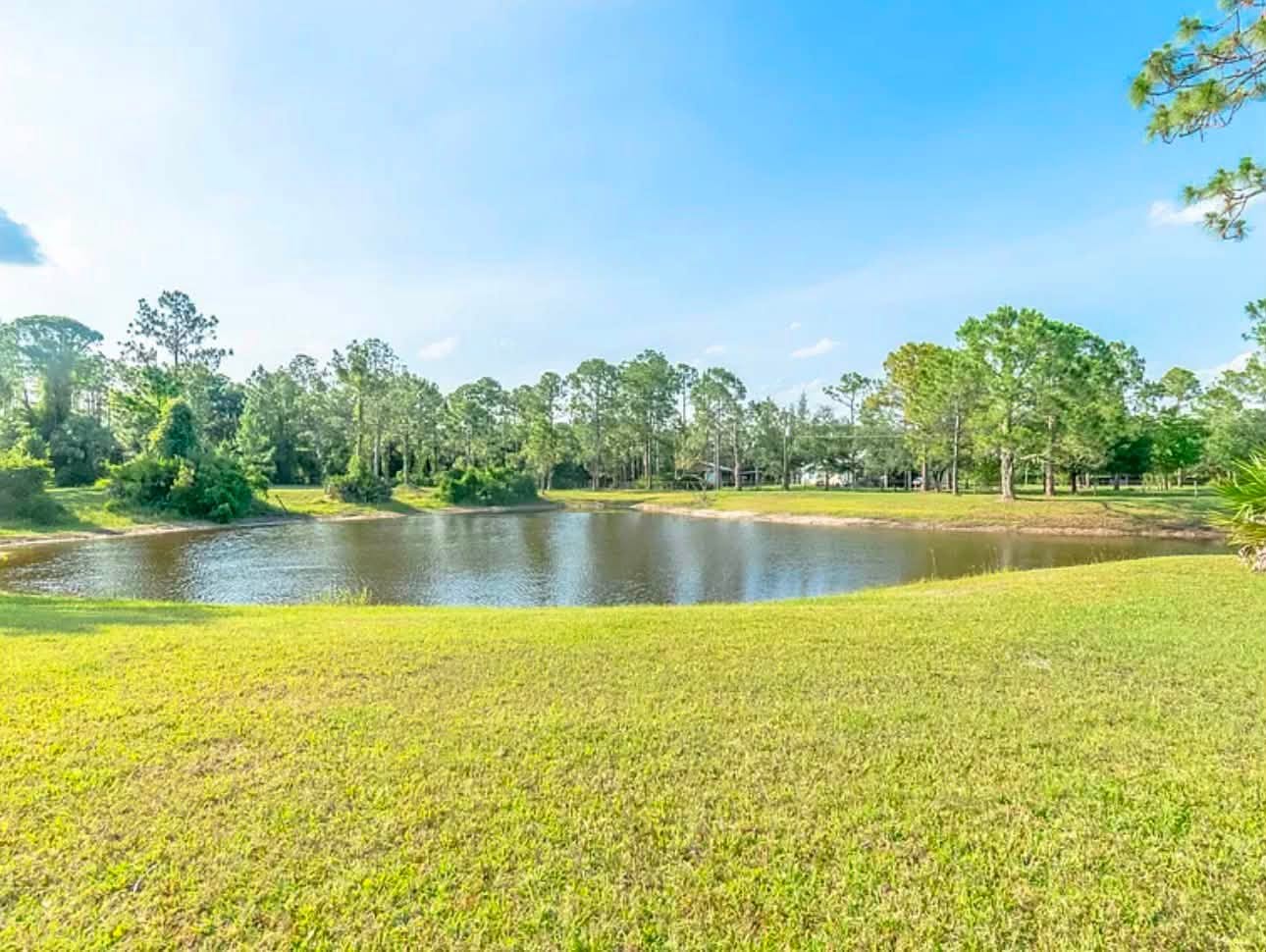 Pond and open green grounds beneath a blue Florida sky